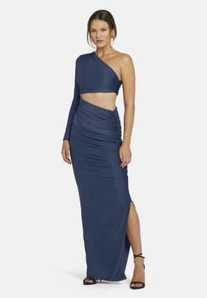 Navyblaues, einseitiges Kleid aus elastischem Stoff, mit Raffung und Schlitzen an der Seite, kombiniert mit schwarzen Riemchensandalen.