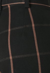 Tissu noir texturé avec des motifs en plaid de couleur cuivre, à la fois verticaux et horizontaux, mettant en avant un gros plan des détails du tissage et des coutures.