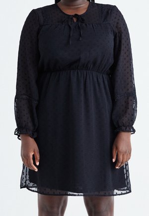 Black knee-length dress with sheer long sleeves and dotted texture, featuring a tied neckline and gathered waist.