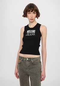 Juodas raštuotas maikutė su "MOSCHINO JEANS" logotipu, derinama su alyvų žaliais kelnais su aukštu juosmeniu, turinčiais tekstūruotą detalę kišenėje.