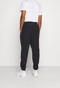 Zwarte joggingsbroeken met elastische tailleband, zijzakken en geribde boorden. Draagt een wit T-shirt en witte sneakers.