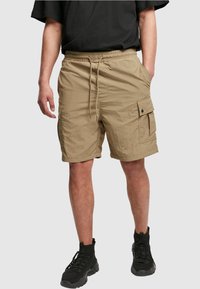 Beige cargo shorts yang terbuat dari kain ringan, dilengkapi dengan pinggang tali serut, saku samping, dan saku tambalan dengan Penutup snap.