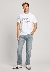 White T-shirt with a blue and red "Pepe Jeans" logo, paired with light blue denim jeans and white sneakers with black accents.