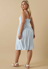 Ljusblå blommig klänning med figurnära överdel, smockad rygg, utsvängd kjol och tunna remmar, parat med vita sandaler med remmar.