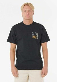 Schwarzes Baumwoll-T-Shirt mit kurzen Ärmeln, ausgestattet mit einem kleinen grafischen Taschendesign in Weiß und Orange, getragen mit beigen Hosen.