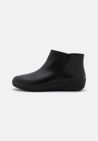 Botas de cuero negro hasta el tobillo con punta redondeada, textura suave y suela de cuña baja. La parte superior presenta un diseño limpio y minimalista.