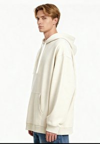 Sudadera de gran tamaño color crema hecha de tela suave, que presenta un bolsillo frontal, capucha con cordón y puños y dobladillo acanalados.