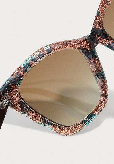 Sonnenbrille mit Katzenaugen-Form, gemustertem Rahmen in Kupfer- und Türkistönen und braunem Verlaufsglas. Strukturiertes Detail entlang der Kanten.