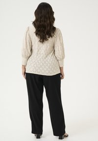 Beżowy sweter z dzianiny w diamentowy wzór i bufiaste rękawy, w zestawie z czarnymi, szerokimi spodniami. Gładka tekstura, krótka długość, casualowy design.