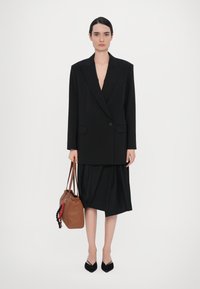 Black oversized blazer with structured shoulders, paired with a black draped skirt. Brown handbag with accent and black pointed flats.