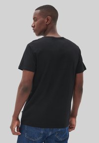 Tricou negru din bumbac, cu mâneci scurte, gât rotund și o croială lejeră. Detalii remarcabile ale cusăturii aproape de tiv. Purtați cu blugi din denim albastru.