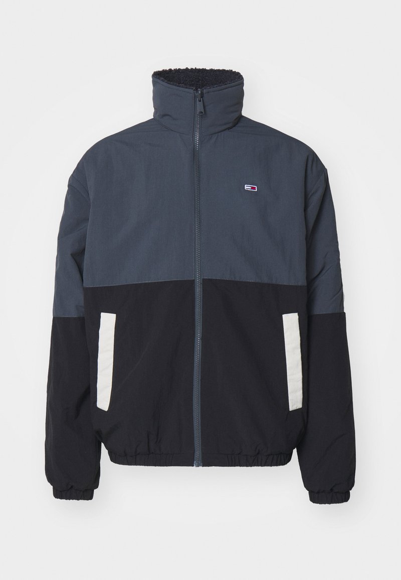 Herrenzipperjacke in dunkelblau, hellblau und schwarzen Farbblöcken. Mit hohem Kragen und elastischen Bündchen, seitlichen Taschen und Logodetail.