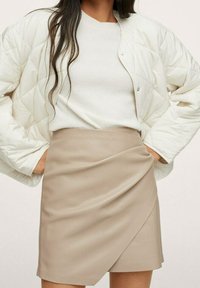 Giacca bianca trapuntata con bottoni automatici, maglione grigio chiaro e gonna avvolgente beige con una morbida consistenza e drappeggio diagonale.