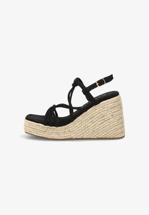 Sandalia cuña negra con tiras, hebilla en el tobillo y suela plataforma de yute natural trenzado, vista lateral sobre fondo blanco.