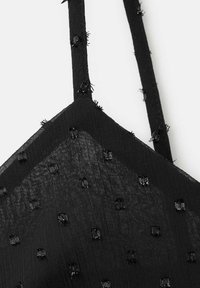 Svart bralette med genomskinligt tyg och fyrkantiga paljetter, justerbara band och en strukturerad yta. Klassisk trekantsform.
