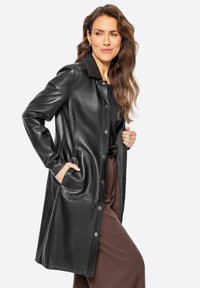 Abrigo de cuero negro con cierre de botón, mangas largas y bolsillos laterales. Textura suave, ajuste entallado y detalle en el cuello.