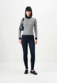 Stripet genser med lange ermer i grå og marineblå, kombinert med mørke skinny jeans. Tilbehøret inkluderer en liten marineblå håndveske og svarte loafers.