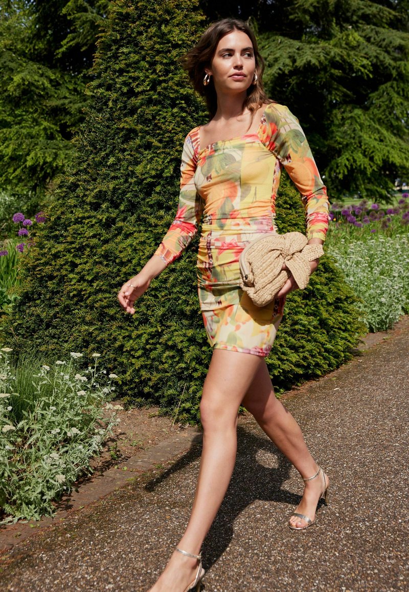 Abito aderente a maniche lunghe con un vivace motivo floreale in tonalità gialle e arancioni. Tessuto strutturato, silhouette bodycon.