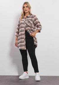 Camicia plaid a quadri rosa e nera con maniche arrotolate, abbinata a leggings neri e sneakers bianche. La camicia ha una vestibilità ampia e spacchi laterali.