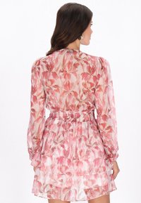 Vestido rosa transparente con patrones florales, cintura fruncida, dobladillo con volantes y mangas largas. La tela suave y ligera realza su diseño fluido.