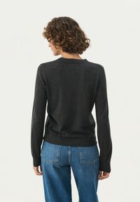 Mørk grå striktrøje med rund hals og lange ærmer, parret med lyseblå højtaljede jeans. Glat tekstur, tætsiddende design.