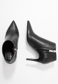 Stivaletti in pelle nera con punta affilata e tacco a stiletto di 10 cm, dotati di chiusura con zip laterale e superficie liscia.