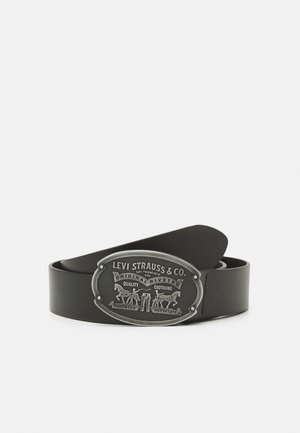 Ceinture en cuir noir roulée avec une boucle ovale en argent ornée du logo Levi Strauss & Co., représentant deux chevaux tirant un jean en denim.
