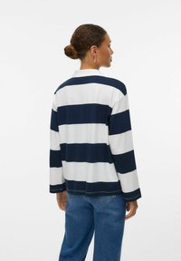 Polo a maniche lunghe a righe blu navy e bianche con colletto, polsini a coste e taglio dritto; abbinato a jeans a vita alta blu chiaro.