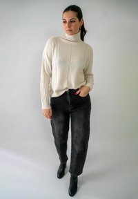 Crème-kleurige gebreide coltrui met geribde mouwen, gecombineerd met hoge zwarte jeans en zwarte enkellaarsjes.