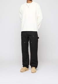 White long-sleeve ribbed shirt, black cargo pants with pockets and silver hardware, beige slip-on shoes. Simple, functional design.