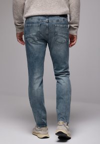 Jeans di denim azzurro chiaro con vestibilità slim, dotati di tasche posteriori e leggera scoloritura. Abbinati a sneakers grigie e a un maglione beige.