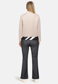 Jasnobeżowa, strukturalna kurtka o dopasowanym kroju, w połączeniu z czarnymi spodniami dzwonami i białymi sneakersami, widok z tyłu.