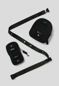 Set di borse in nylon nero composto da una borsa principale con due cinture in pelle, una borsa più piccola e una cinghia con testo in rilievo e una fibbia in metallo.