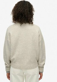 Beige oversized sweater met een geribbelde rand en boorden, gemaakt van zacht materiaal. Toon de achterkant, waardoor een ontspannen pasvorm en verlaagde schouders zichtbaar zijn.