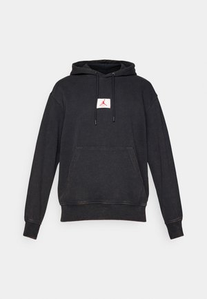 Felpa nera con cappuccio, dotata di tasca frontale e logo Jumpman rosso su una toppa bianca centrata sul petto, esposta su uno sfondo bianco.