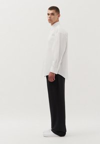 Witte blouse met lange mouwen, ontspannen pasvorm, enkele borstzak. Gecombineerd met zwarte wijde pantalon en witte sneakers.