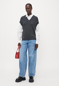 Grå strikket vest over en hvit skjorte, sammen med lyseblå vide jeans, svarte klumpete sko og en liten rød håndveske.