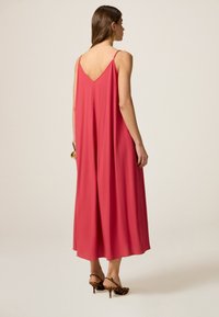 Rochie lungă și vaporoasă din material coral, cu un design cu spate în V și bretele subțiri, având o croială lejeră care ajunge până la glezne.