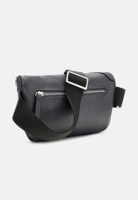 Bolso cruzado negro texturizado con compartimentos con cremallera, correa de tela ajustable y acentos de hardware plateado. Diseño rectangular.