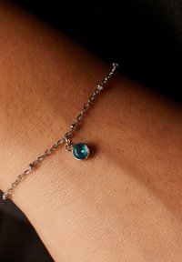 Zilveren schakelarmband met een kleine blauwe edelsteen pendant, met een ronde vorm en gepolijste oppervlakte, weergegeven op huid.