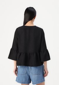 Black peplum top with a textured fabric, flared sleeves, and a round neckline, paired with light blue denim shorts.
