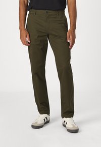 Olivgröna byxor i bomullstwill, med rak bendesign, enkel knappstängning och två sidofickor. Accenterade med svarta skor.