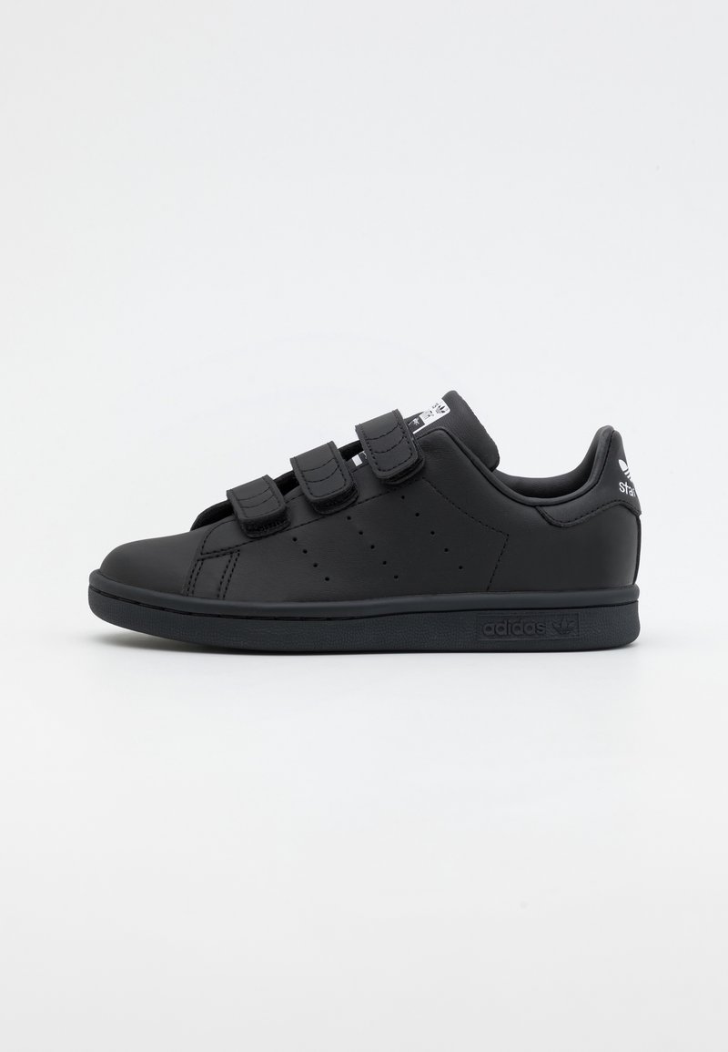 Black sneakers with a smooth, matte leather texture, featuring three Velcro straps and perforated detailing on the sides.