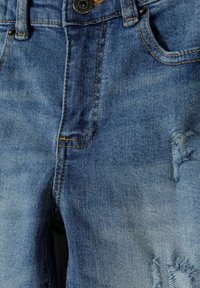 Jeans de mezclilla azul con un acabado desgastado, lavado claro, costuras en contraste y un bolsillo frontal con cierre de botón.