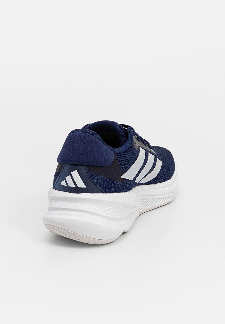Zapatilla deportiva azul marino con un upper de tela texturizada, tres rayas blancas en el costado y una suela blanca de goma. Talón acolchado para mayor comodidad.