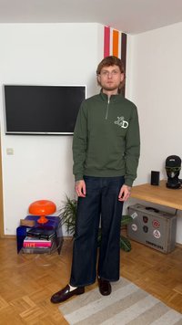 Felpa verde con zip e dettaglio del logo, abbinata a jeans a gamba larga blu scuro e scarpe bordeaux. Tessuto strutturato e vestibilità rilassata.