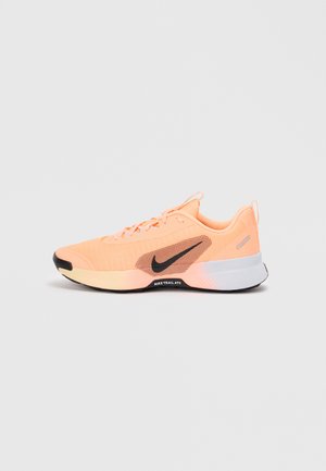 Nike løbesko med en let ferskenfarvet mesh-overdel, tekstureret panelering, sort swoosh-detalje og en hvid polstret sål med en sort ydersål.
