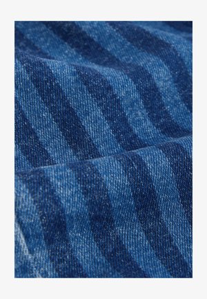 Tissu en denim de différentes nuances de bleu avec un motif discret à rayures. La texture semble solide, avec un tissage classique caractéristique du denim.
