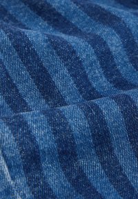 Tissu en denim de différentes nuances de bleu avec un motif discret à rayures. La texture semble solide, avec un tissage classique caractéristique du denim.