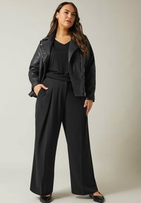 Zwarte leren motorjack over een zwarte V-hals top, gecombineerd met zwarte wijde broek en zwarte loafers, met een relaxte pasvorm en een soepele textuur.